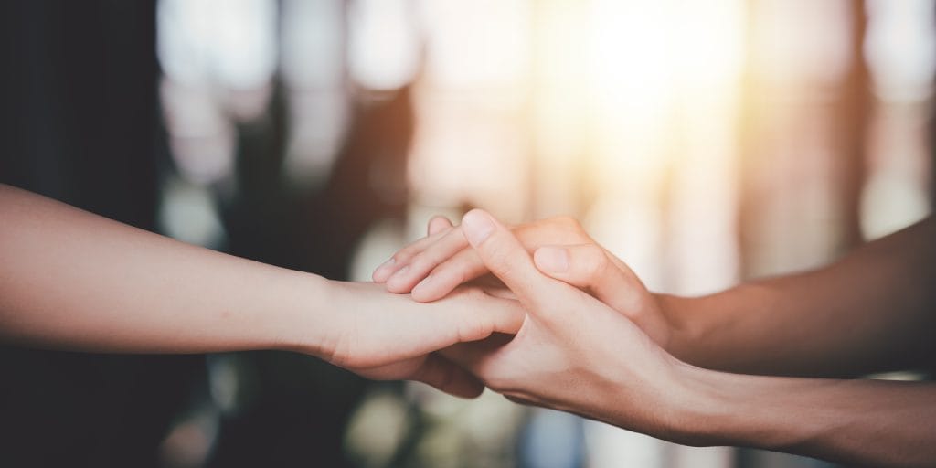 Two hands clasped together, showing support and comfort.
