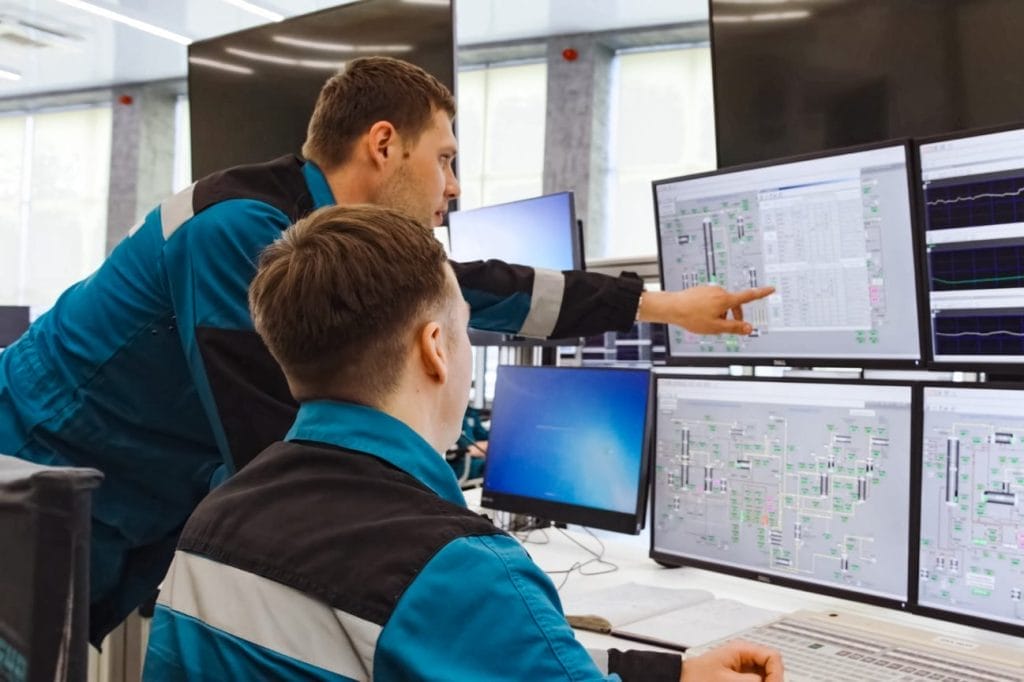 Two engineers collaborate, reviewing industrial process control system displays.