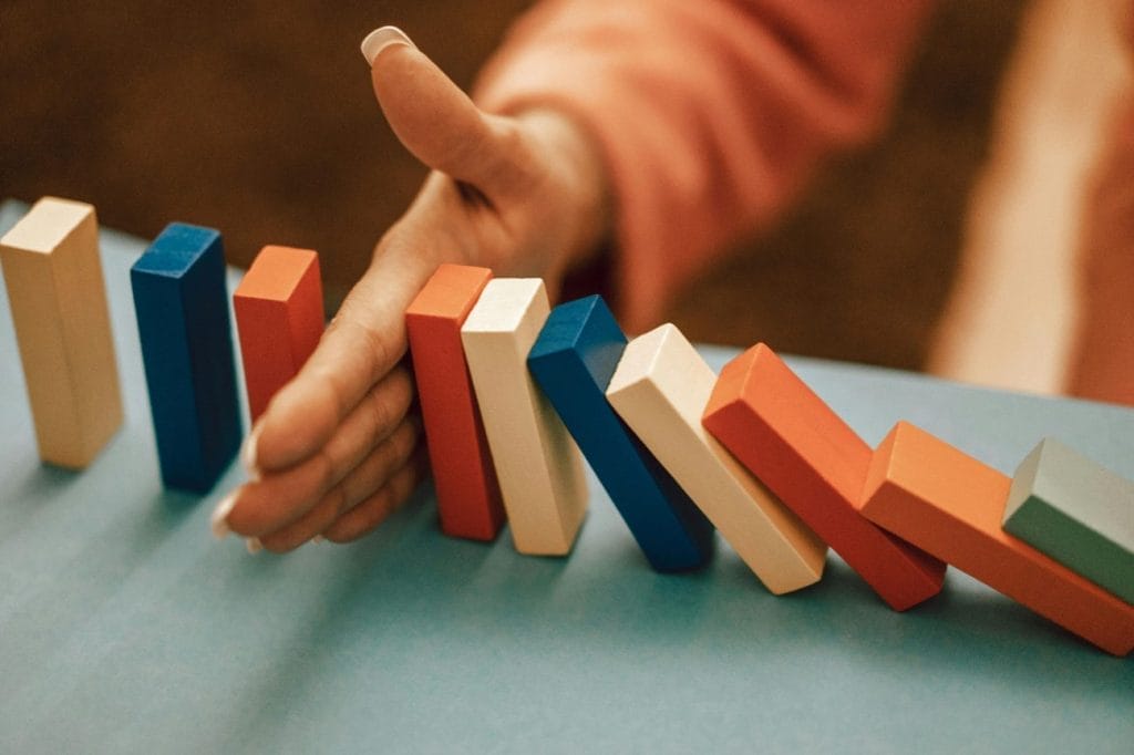 Hand stopping colorful dominoes from falling. Risk management concept.
