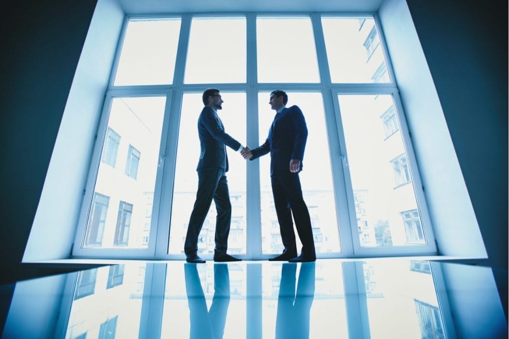 Two businessmen shaking hands in front of a large window.