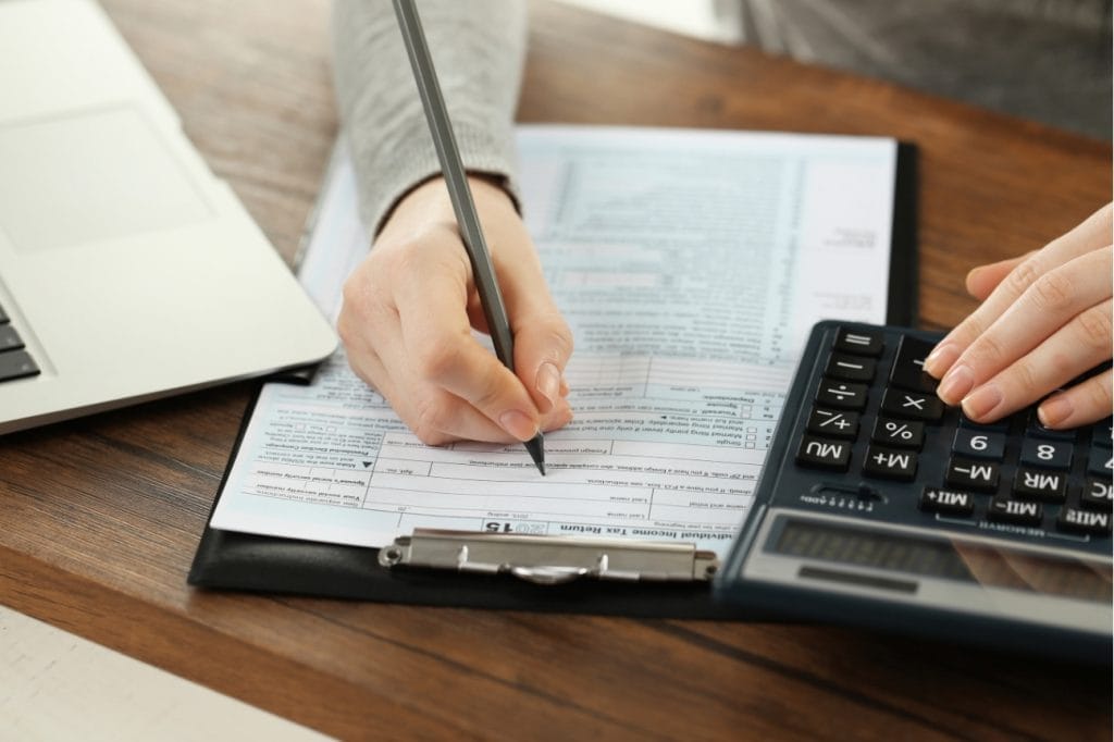 Person completing tax form 1040 using calculator and pencil.