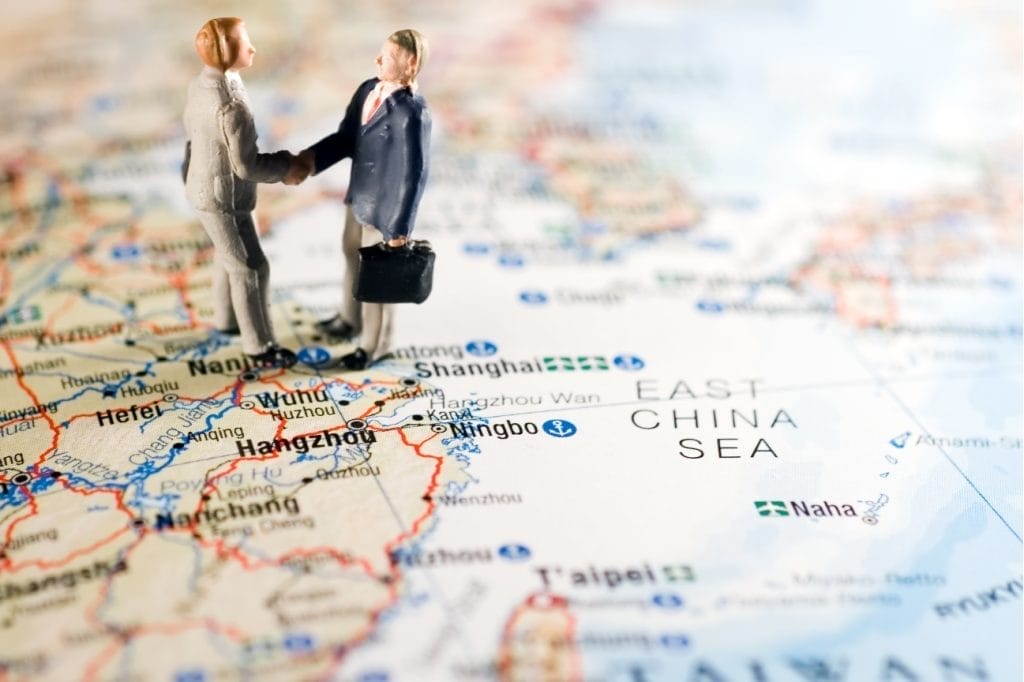 Miniature figures shaking hands over a map of China, symbolizing international business.