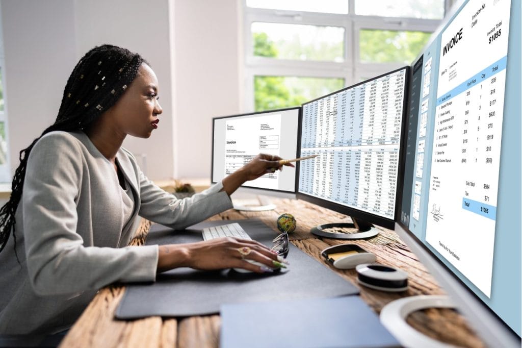 Accountant reviewing invoices and financial data on multiple computer screens.