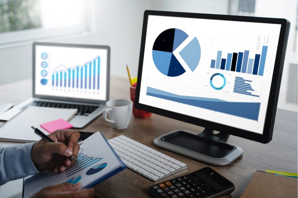 Person reviewing financial data on laptop and desktop computer screens.