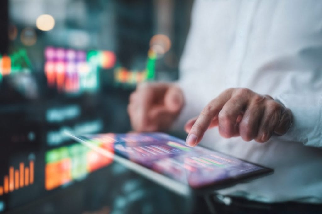 Person using a tablet to monitor business partner portfolio load, with charts and graphs displayed.
